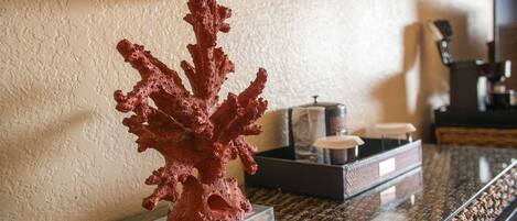A coral sculpture on a clear glass stand on a marble table, with a lamp and a tray of items in the background.
