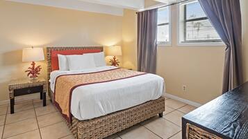 A hotel room with a large bed, two bedside tables with lamps, a wicker chair, and a window with curtains.