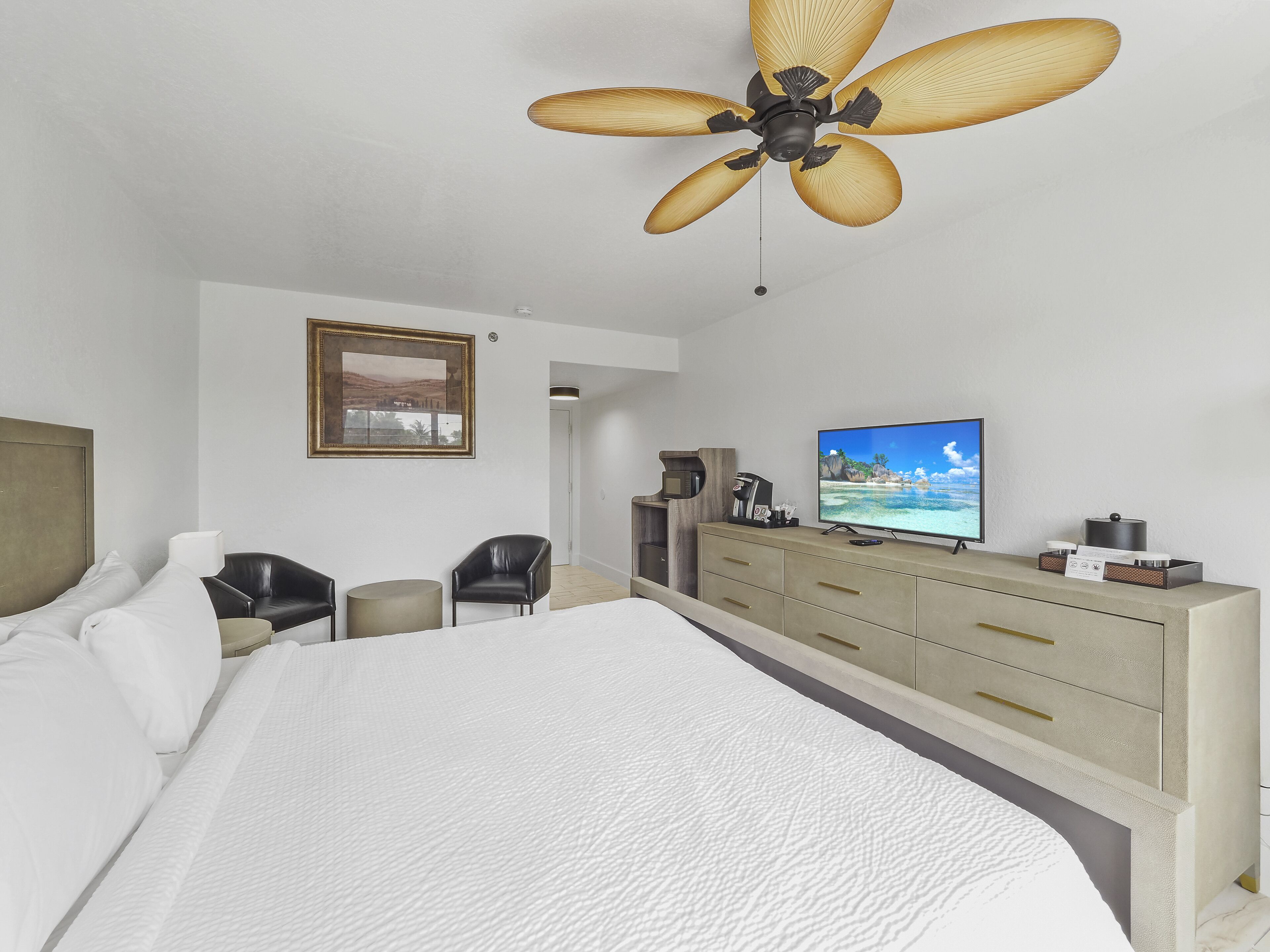 Een hotelkamer met een groot bed, een televisie, een bureau met een computer en een plafondventilator.