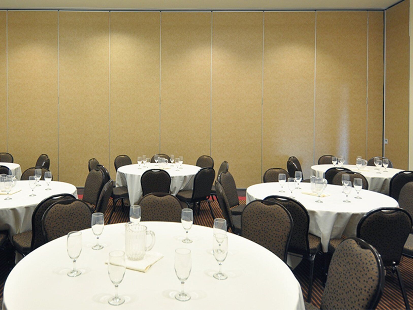 A conference room with multiple round tables, each set with chairs and empty wine glasses.