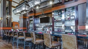 A bar area with leather chairs, a bar counter, and shelves stocked with bottles and glasses. - Overton Hotel and Conference Center (Lubbock)