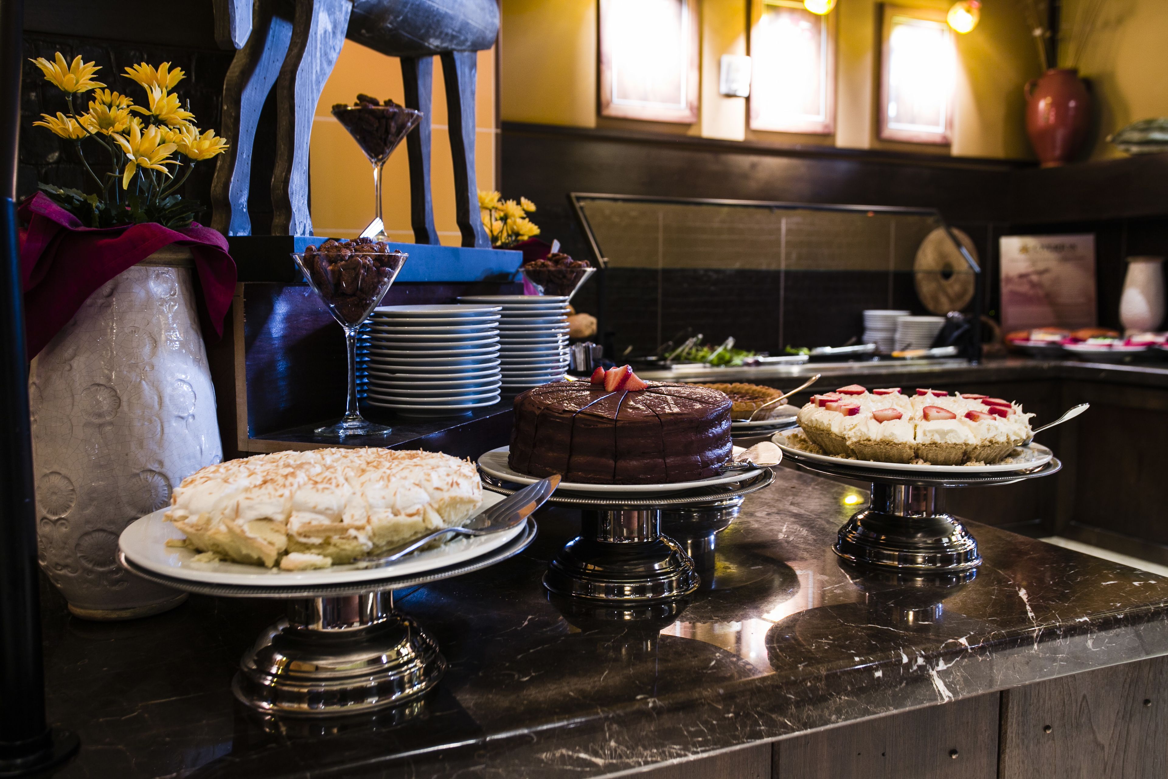 Un mostrador de buffet con diversos postres y un jarrón decorativo con flores amarillas.
