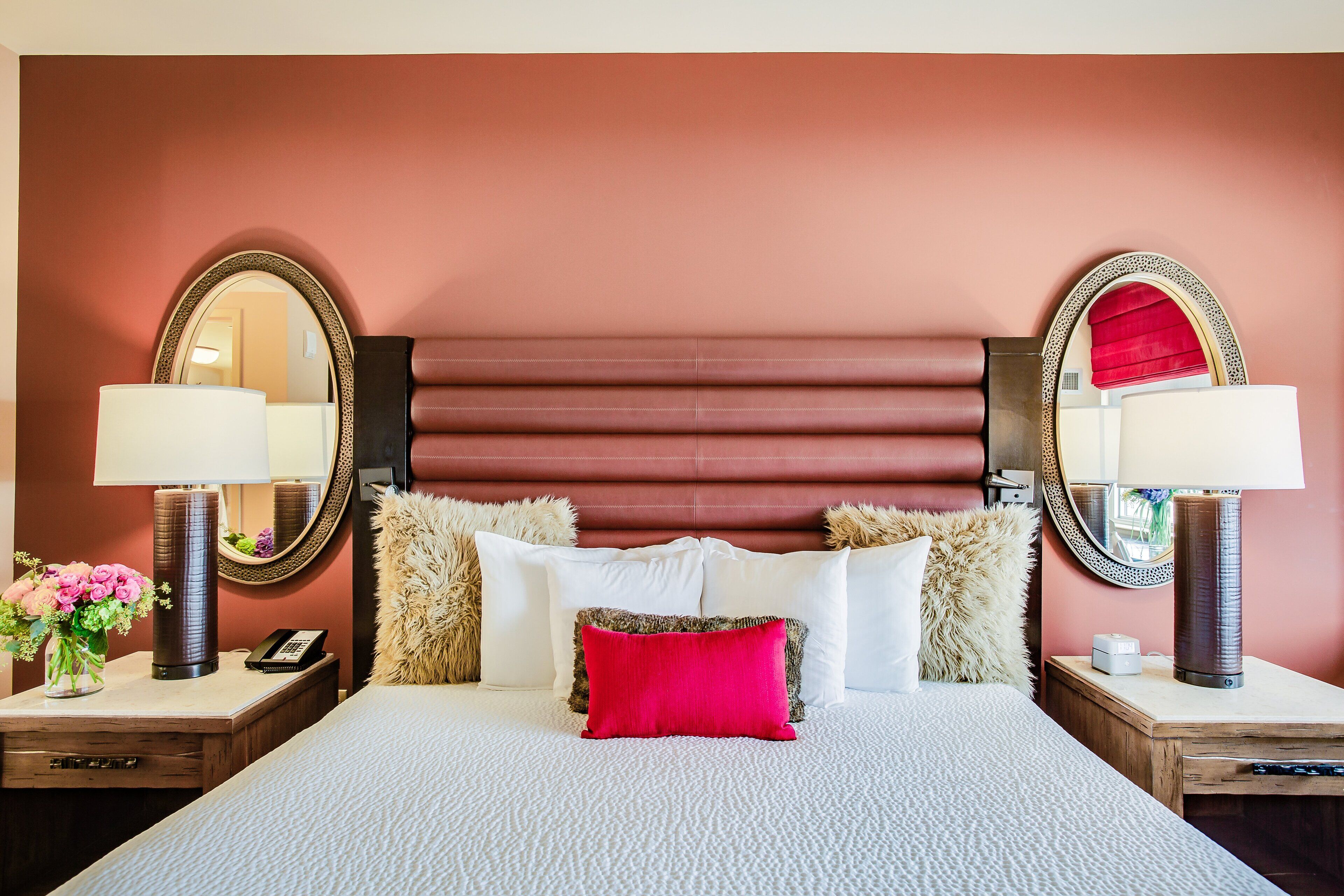 Une chambre d’hôtel avec un grand lit, deux tables de chevet, un miroir et un oreiller rouge.