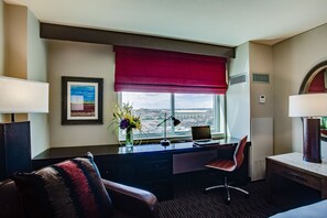 A hotel room with a desk, chair, and a large window with a view of a cityscape.