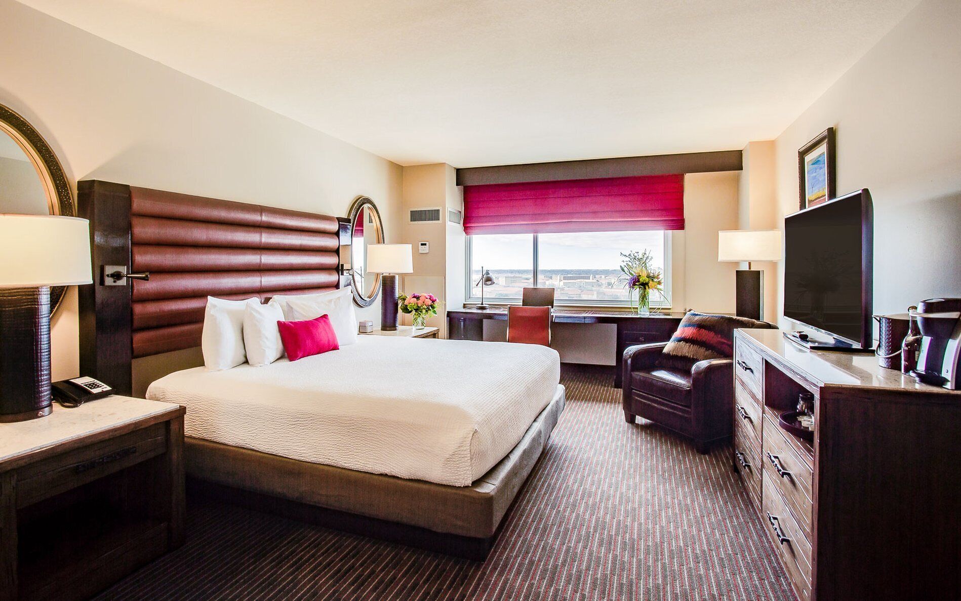 A hotel room with a large bed, a desk, a TV, and a view of the city.
