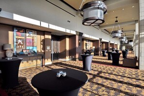 A hotel lobby with patterned carpet, black round tables, and modern pendant lighting.