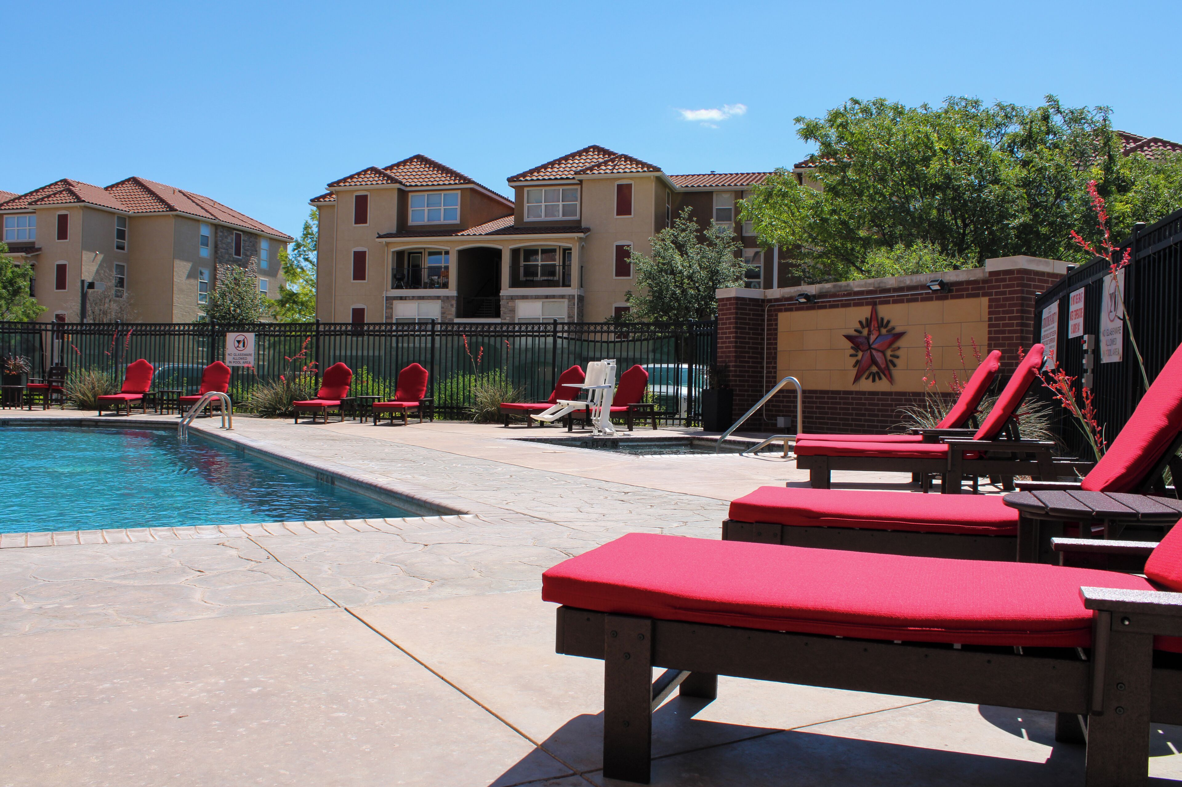 A pool area with red lounge chairs and a brick wall with a star design.