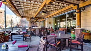 An outdoor patio with wooden tables and chairs, a brick wall, and large windows. - Overton Hotel and Conference Center (Lubbock)