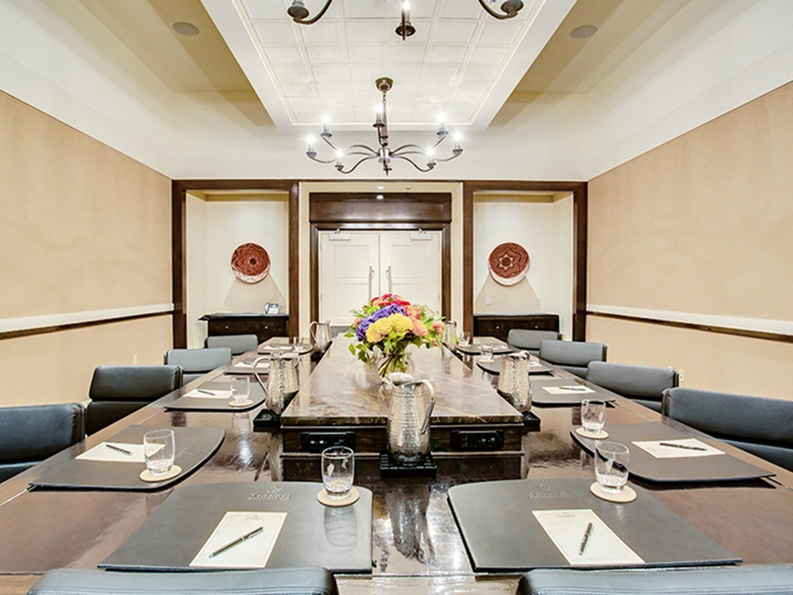 Uma sala de conferências com uma mesa comprida, várias cadeiras, um candelabro e painéis decorativos na parede.