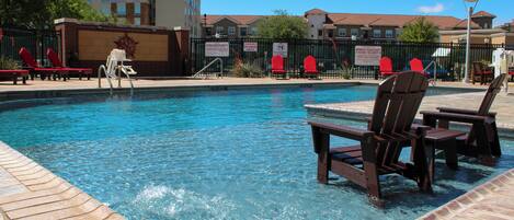 A swimming pool with clear blue water, surrounded by lounge chairs and a brick deck.