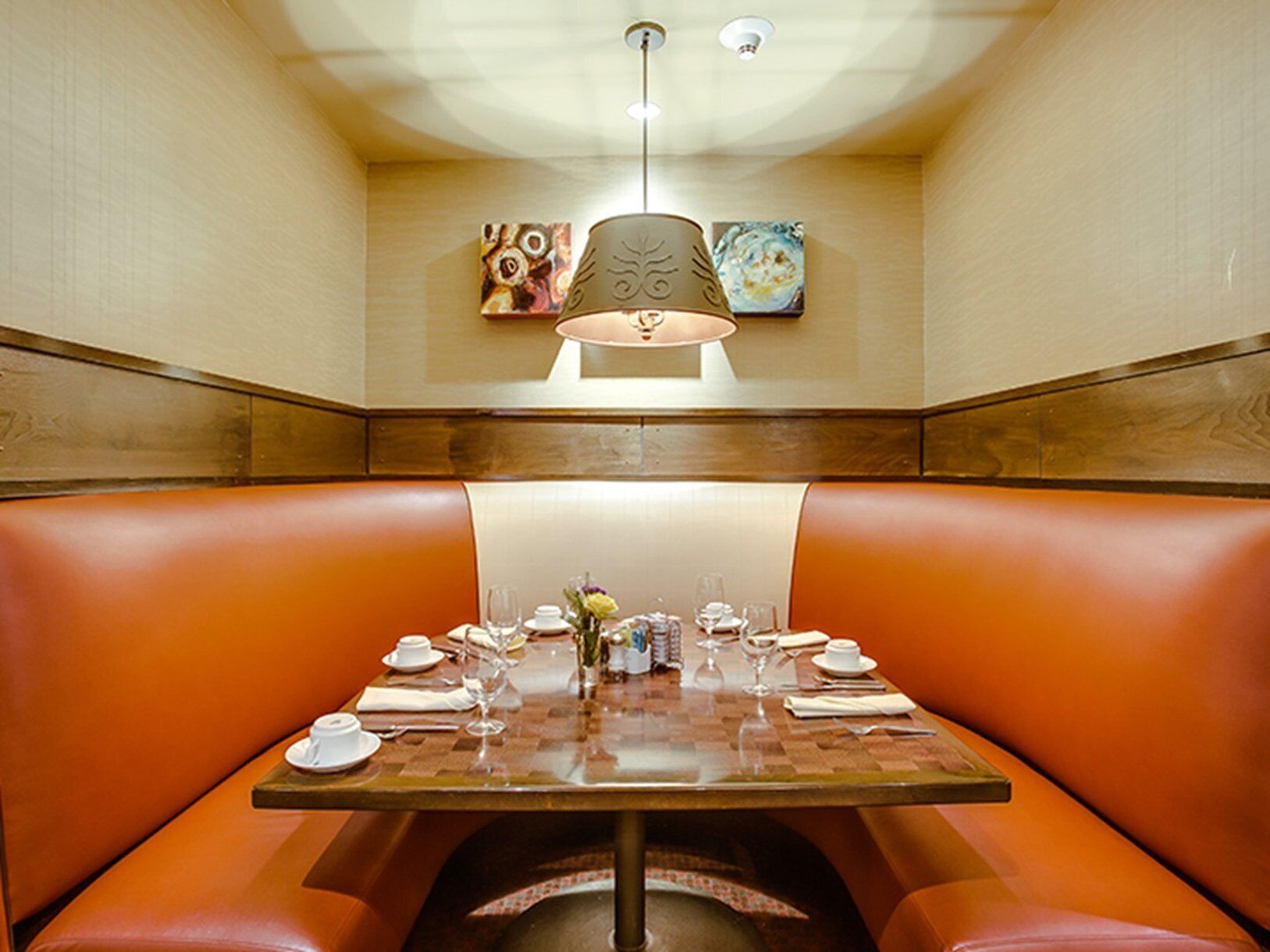 A restaurant with a booth seating arrangement, a table set for dining, and artwork on the walls.