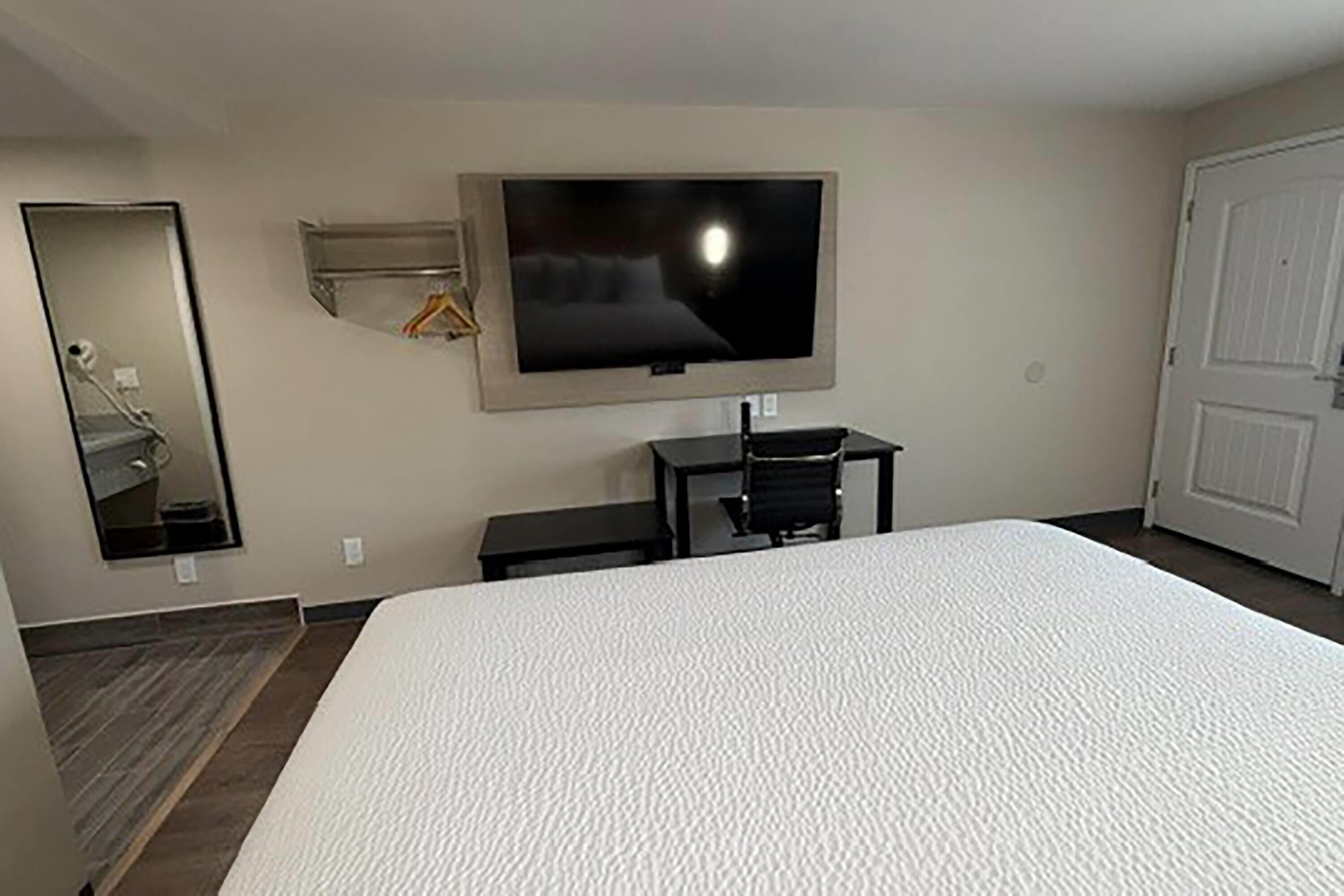 A hotel room with a large bed, a TV mounted on the wall, a desk, and a mirror.