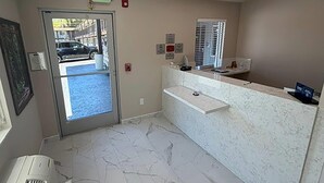A reception area with a marble floor, a reception desk, a window with blinds, and an exit sign. - Travelodge by Wyndham Ukiah (Ukiah)