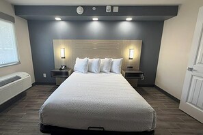 Una habitación de hotel con una cama grande, dos mesitas de noche, un calentador y una ventana.