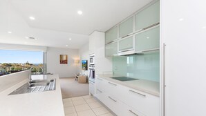 Cozinha moderna com uma ilha grande, eletrodomésticos de aço inoxidável e vista para o exterior.