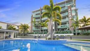 Hotel com piscina, palmeiras e céu azul límpido.