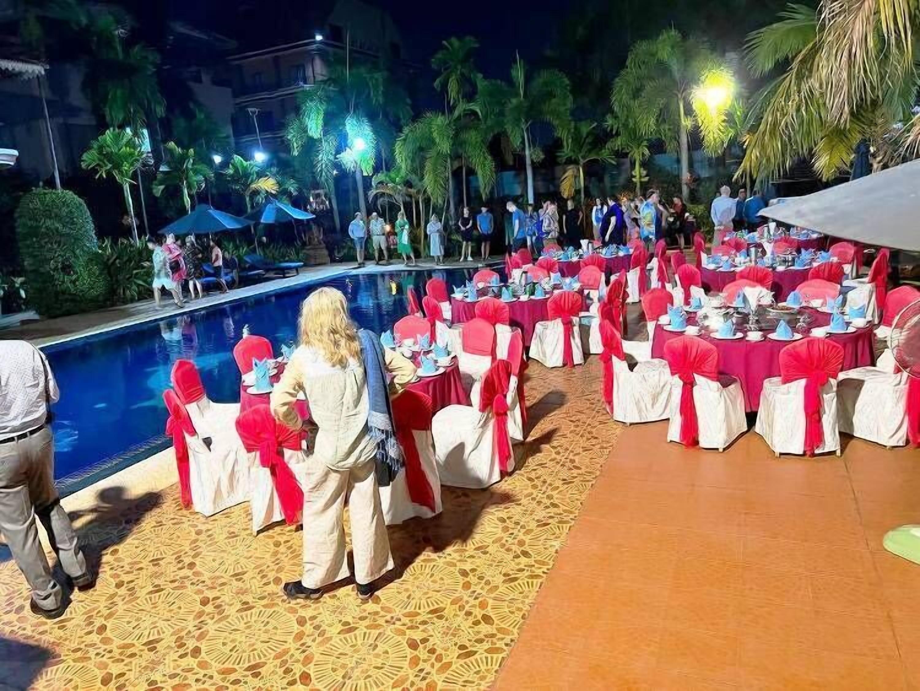 Evento al aire libre con mesas redondas dispuestas para comer, rodeado de sillas con cintas rojas.