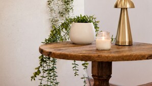 A room with a round wooden table, a potted plant, a candle, and wall-mounted wooden and woven items. - Bay Haven Lodge (Byron Bay)