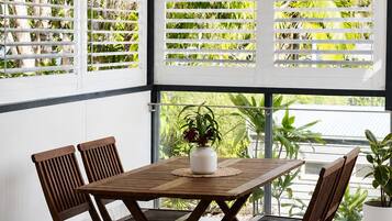 A room with a wooden table and chairs, large windows with blinds, and a ceiling fan.