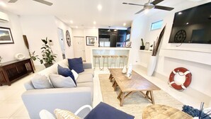 A modern living room with a sofa, coffee table, and dining table. There is a kitchen in the background with bar stools. - Bay Haven Lodge (Byron Bay)