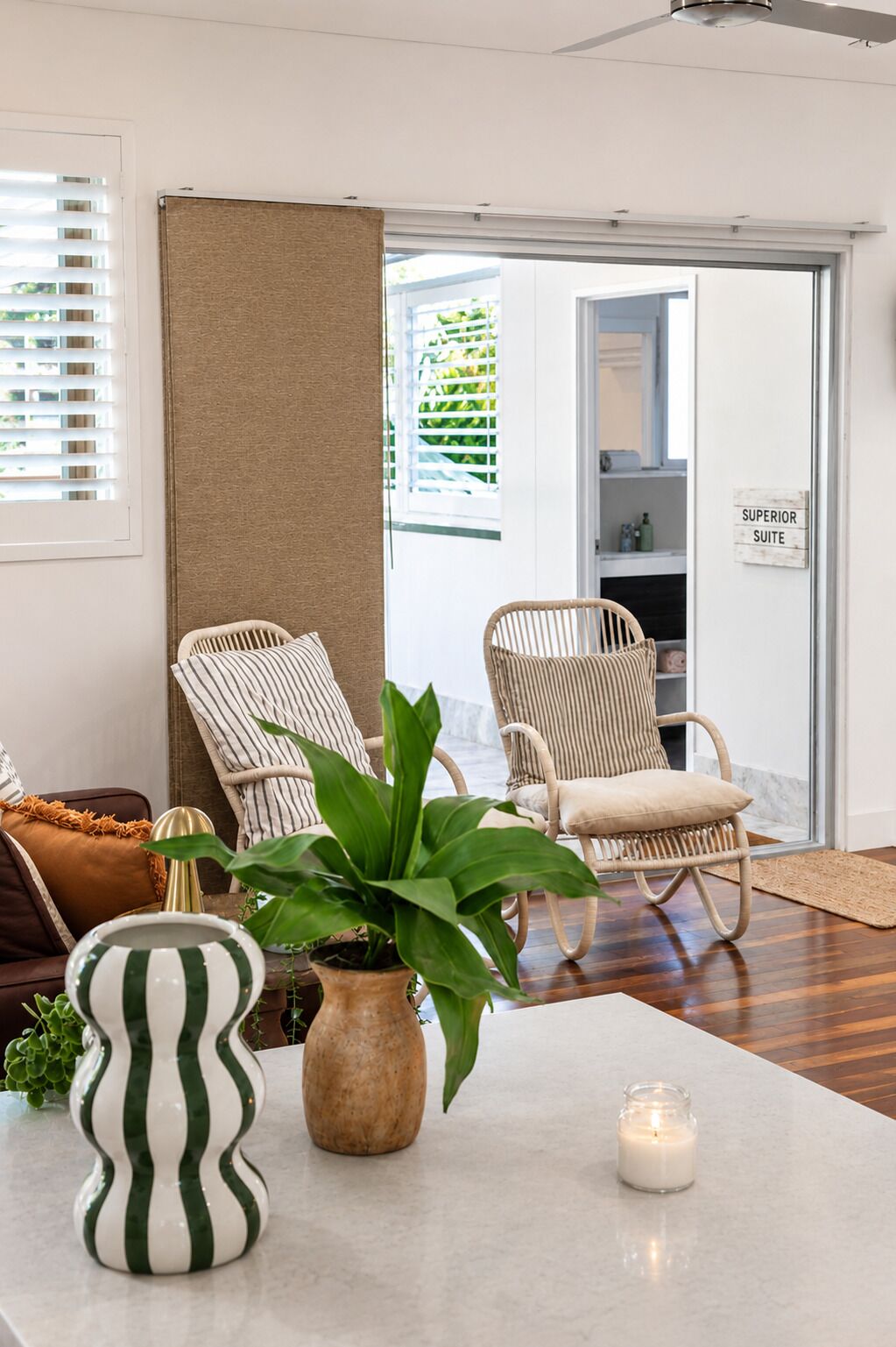 A modern living room with wicker chairs, a striped vase, a potted plant, and a lit candle on a marble table.