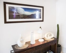 Fotografía enmarco de un rayo sobre un paisaje montañoso, una lámpara blanca, un florero blanco y un cactus sobre una consola de madera.