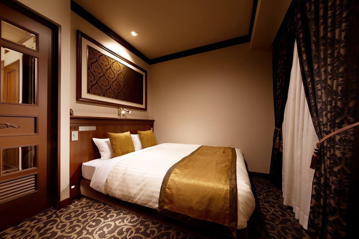 A hotel room with a large bed, a wooden wardrobe, a mirror, and a patterned carpet.