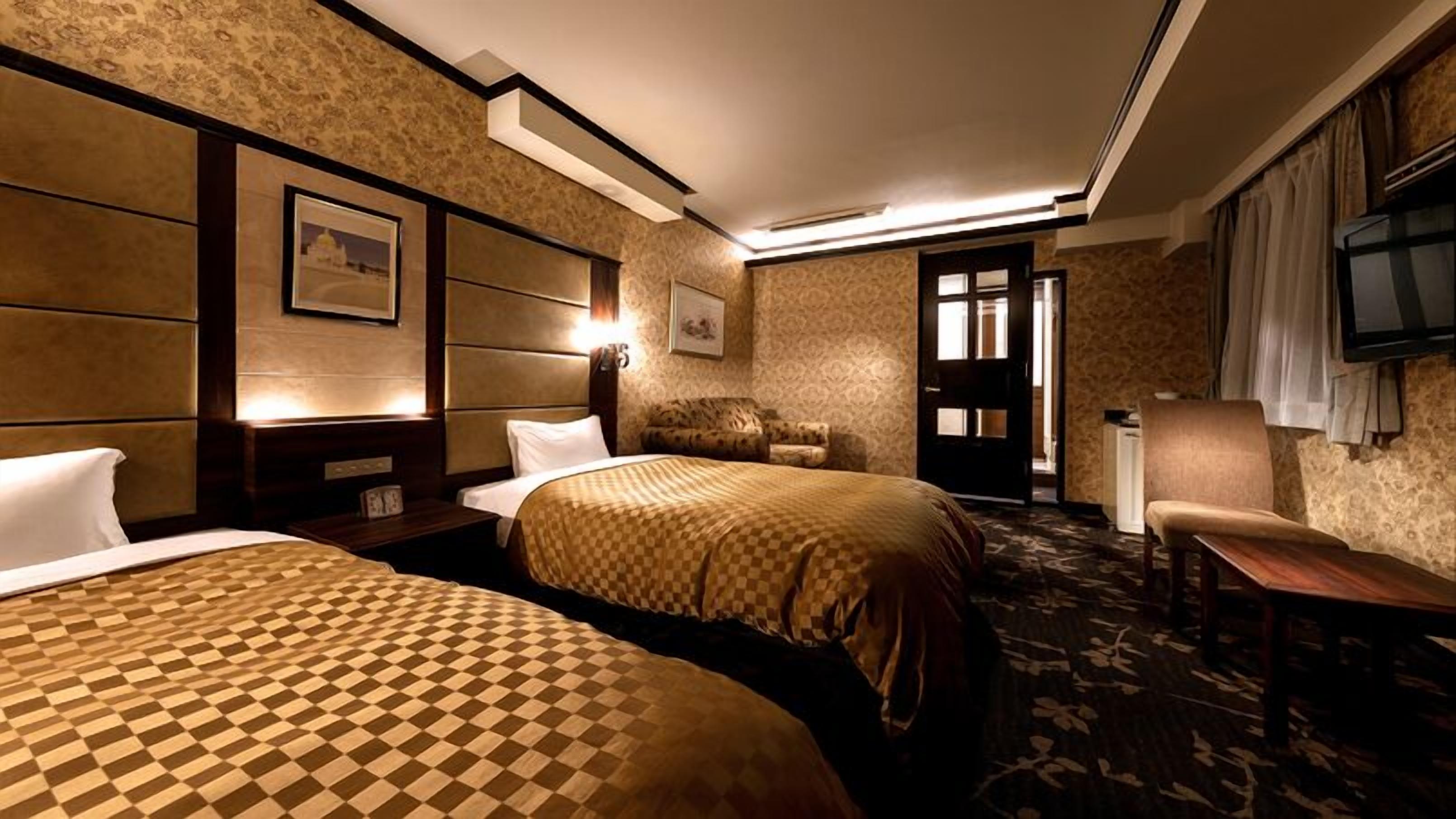 Habitación de hotel con dos camas, un sofá, un televisor y una puerta que da a un baño.
