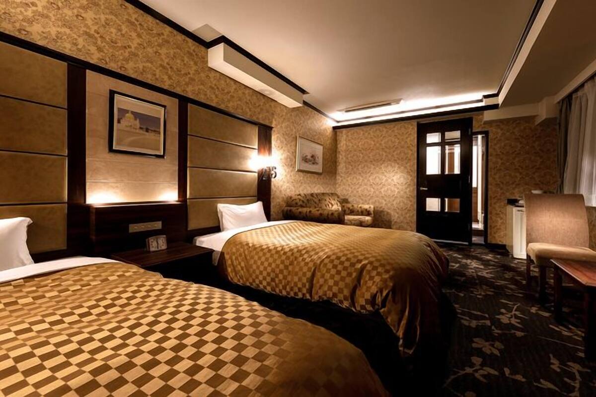 A hotel room with two beds, a sofa, a TV, and a door leading to a bathroom.