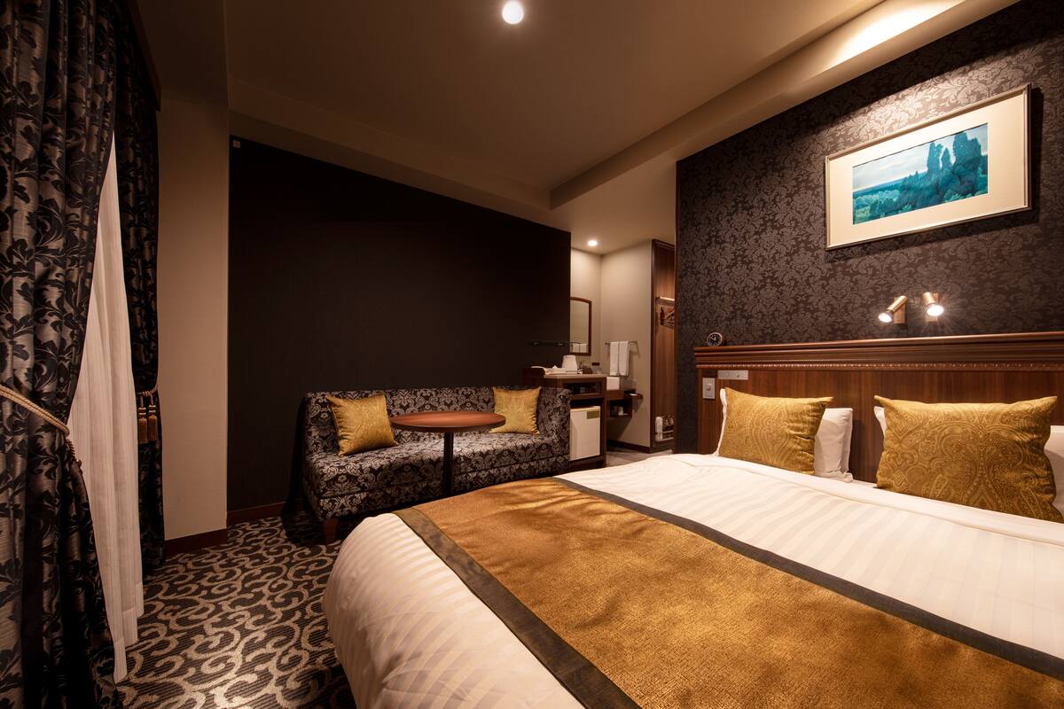 A hotel room with a large bed, a sofa, a small table, and a painting on the wall.