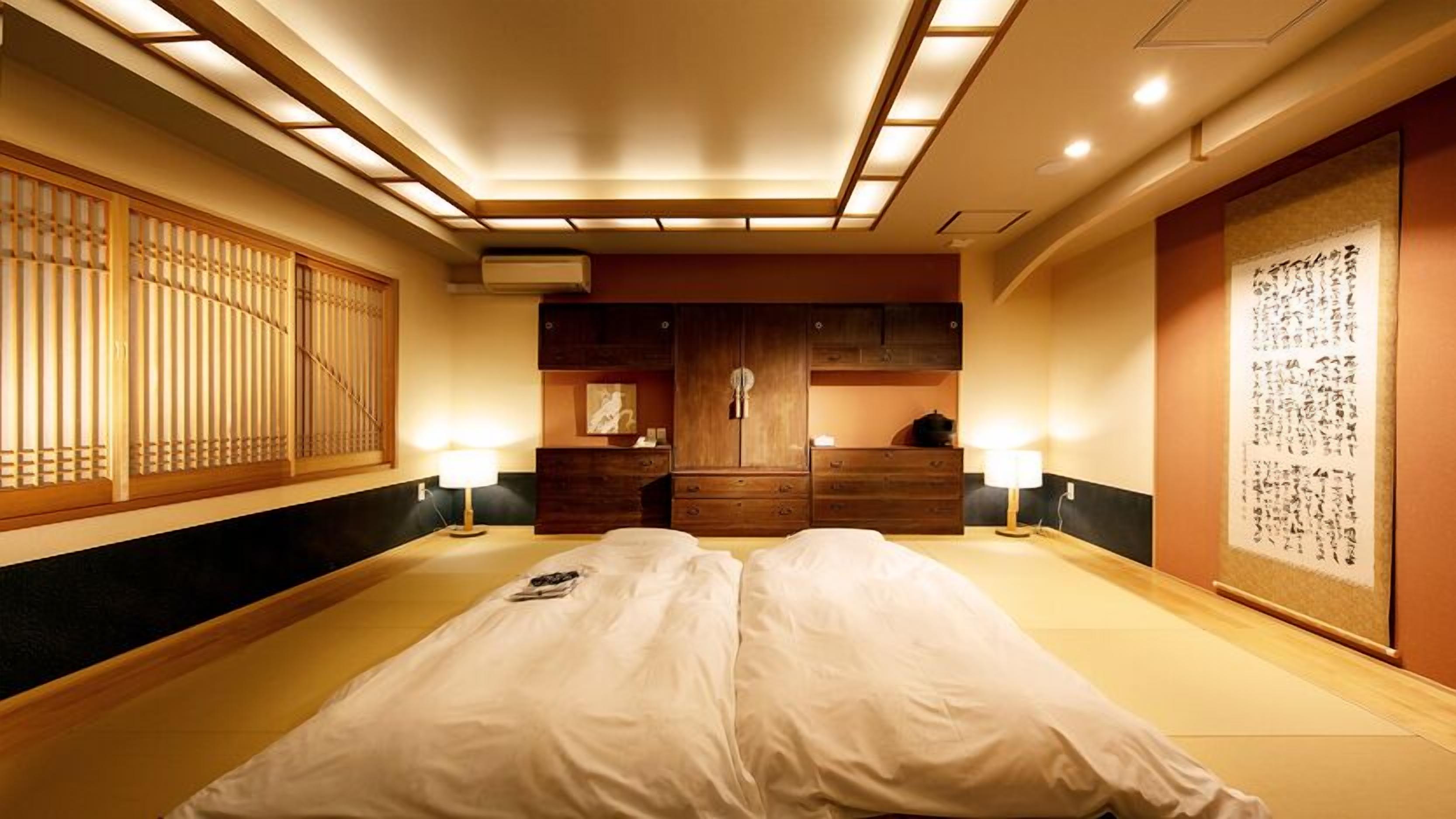 Un dormitorio de estilo japonés tradicional con suelo de tatami, futón, armarios de madera y un biombó shoji.