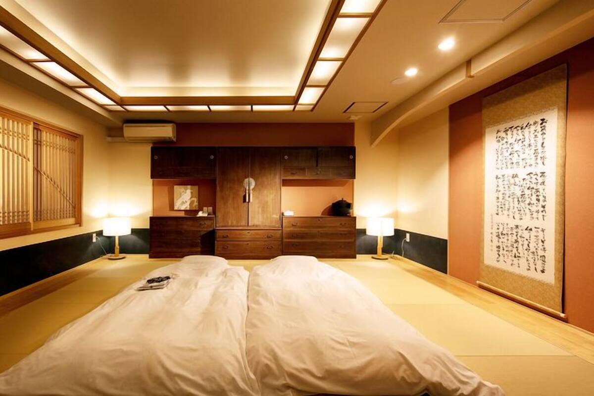 A traditional Japanese-style bedroom with tatami flooring, a futon bed, wooden cabinets, and a shoji screen.