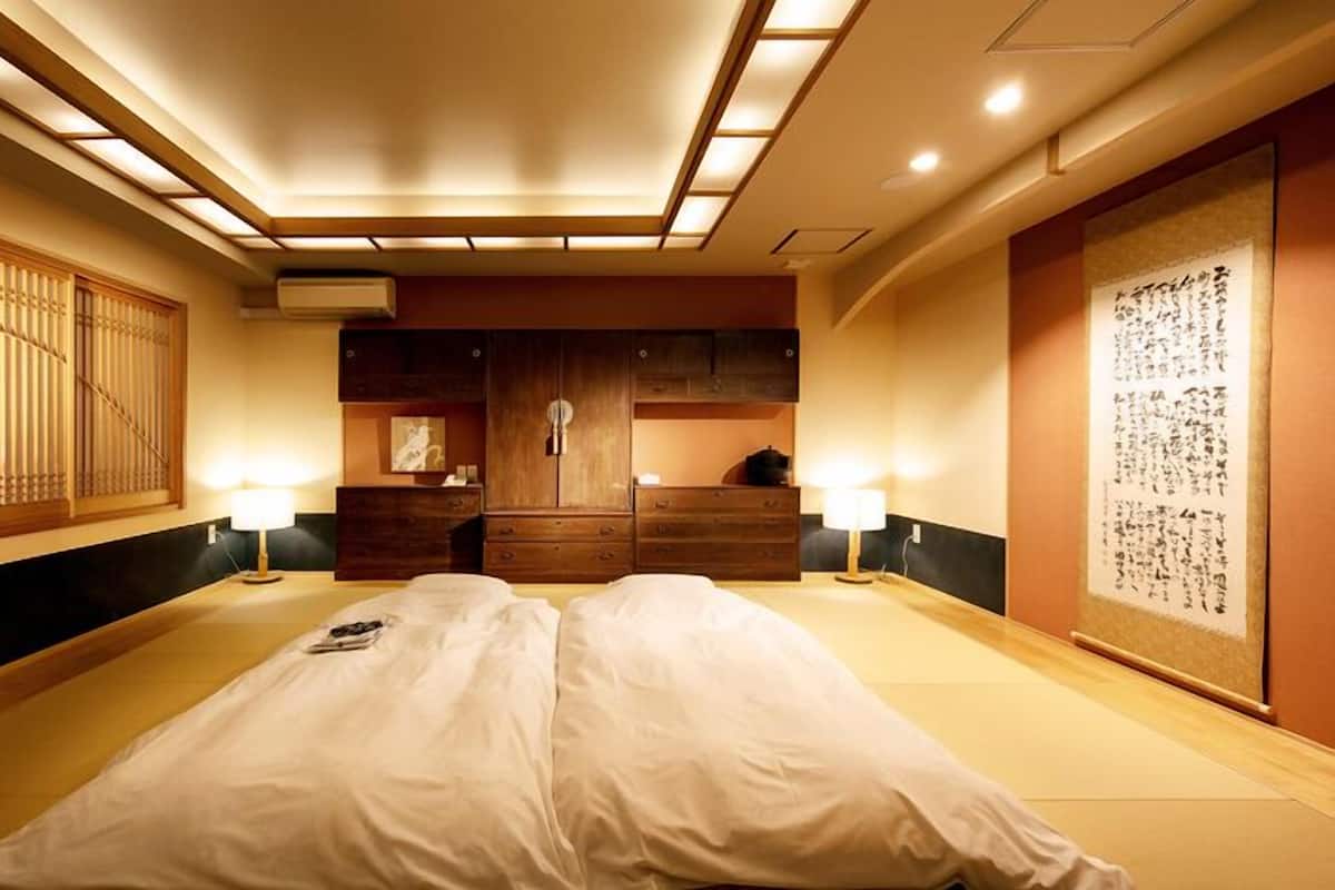 Un dormitorio de estilo japonés tradicional con suelo de tatami, futón, armarios de madera y un biombó shoji.