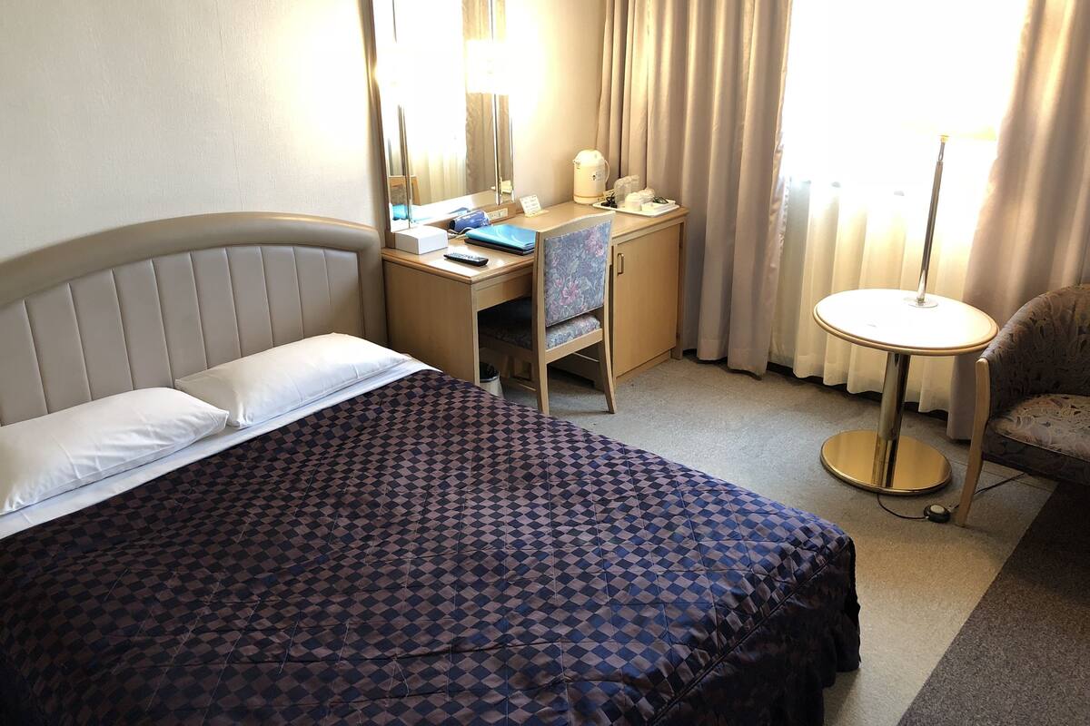 A hotel room with a bed, a desk, a chair, a round table, and a large mirror.