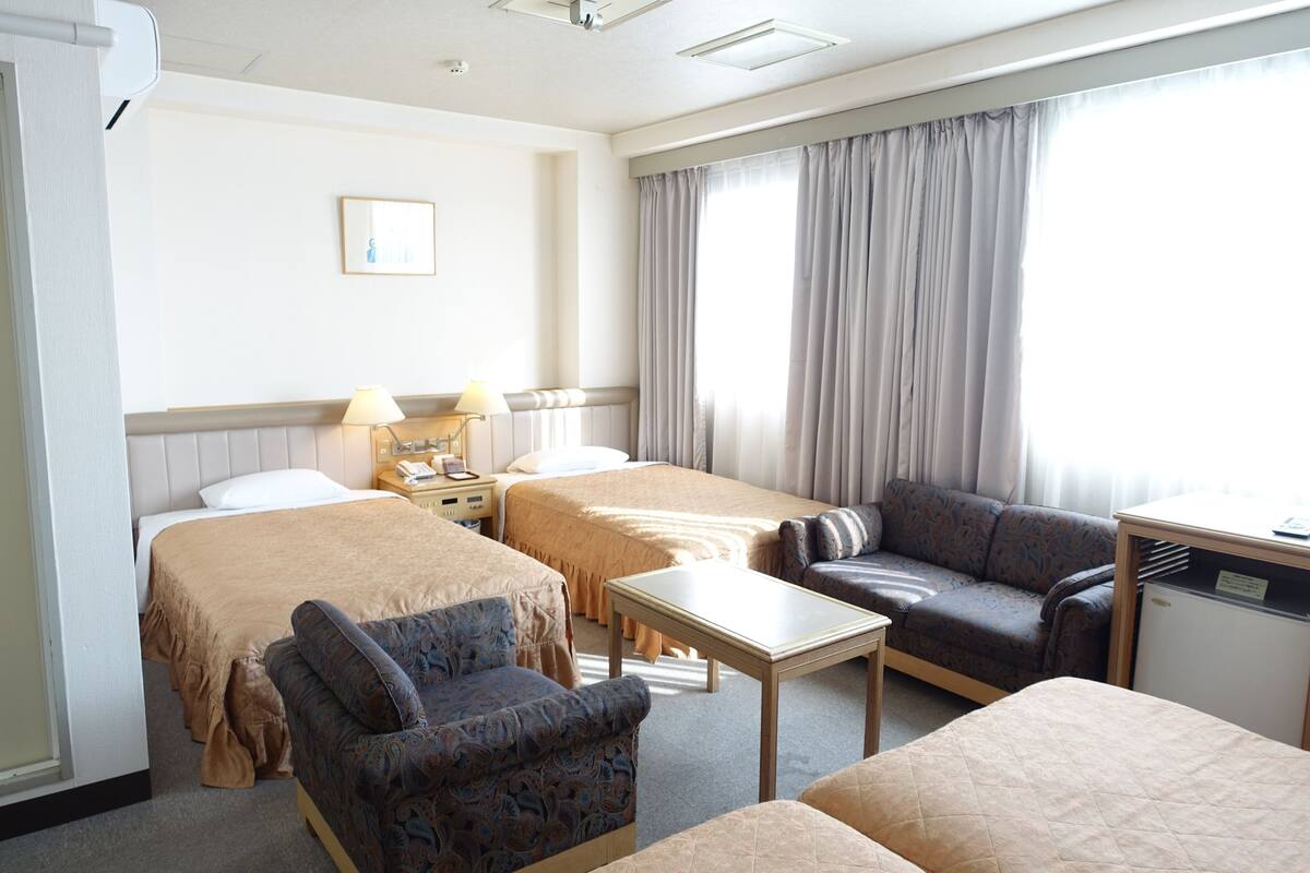 A hotel room with two beds, a sofa, a small table, a desk, and a nightstand with lamps.