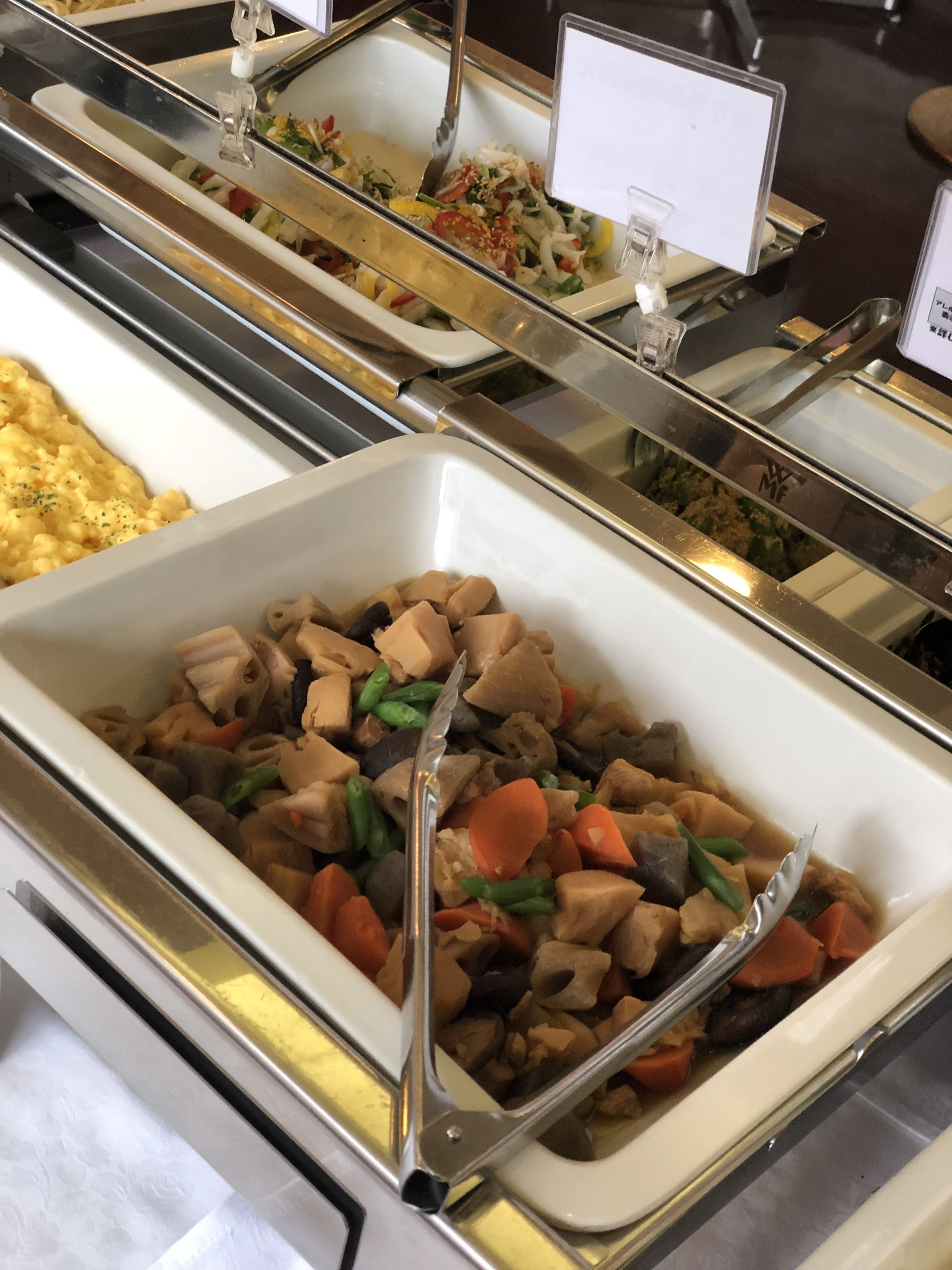 A buffet with various dishes, including a section with a mix of vegetables and meat, and another with scrambled eggs.