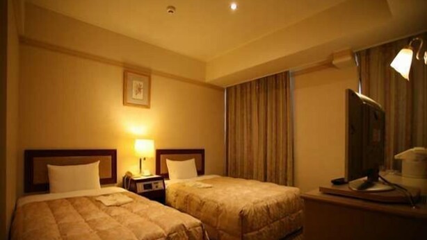 Une chambre d’hôtel avec deux lits, un bureau équipé d’un ordinateur, une lampe et un téléviseur.