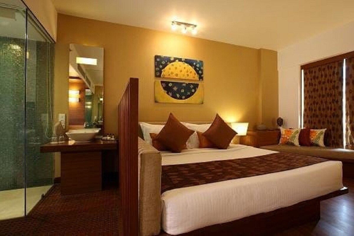 A hotel room with a large bed, a bedside table, a mirror, and a window with curtains.