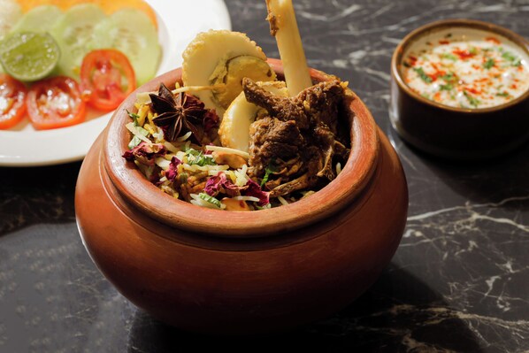 Una olla de barro llena de un guiso con carne, verduras y hierbas.