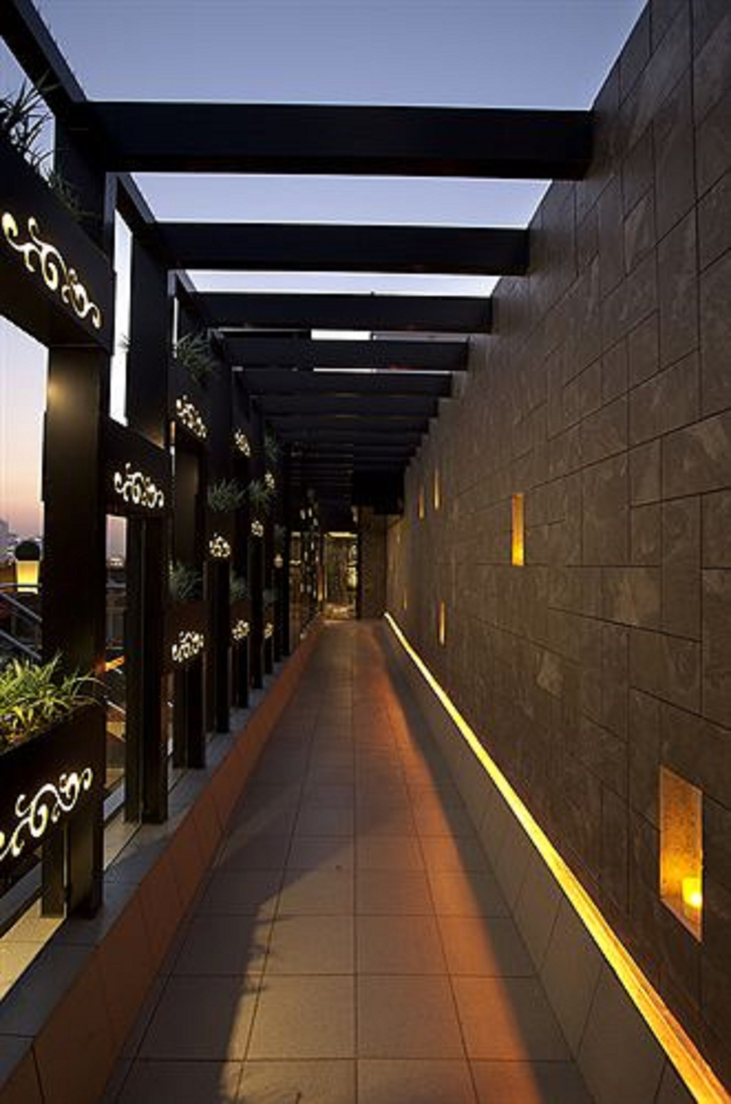 A corridor with a tiled floor, a dark wall with small illuminated panels, and a black structure with decorative elements.