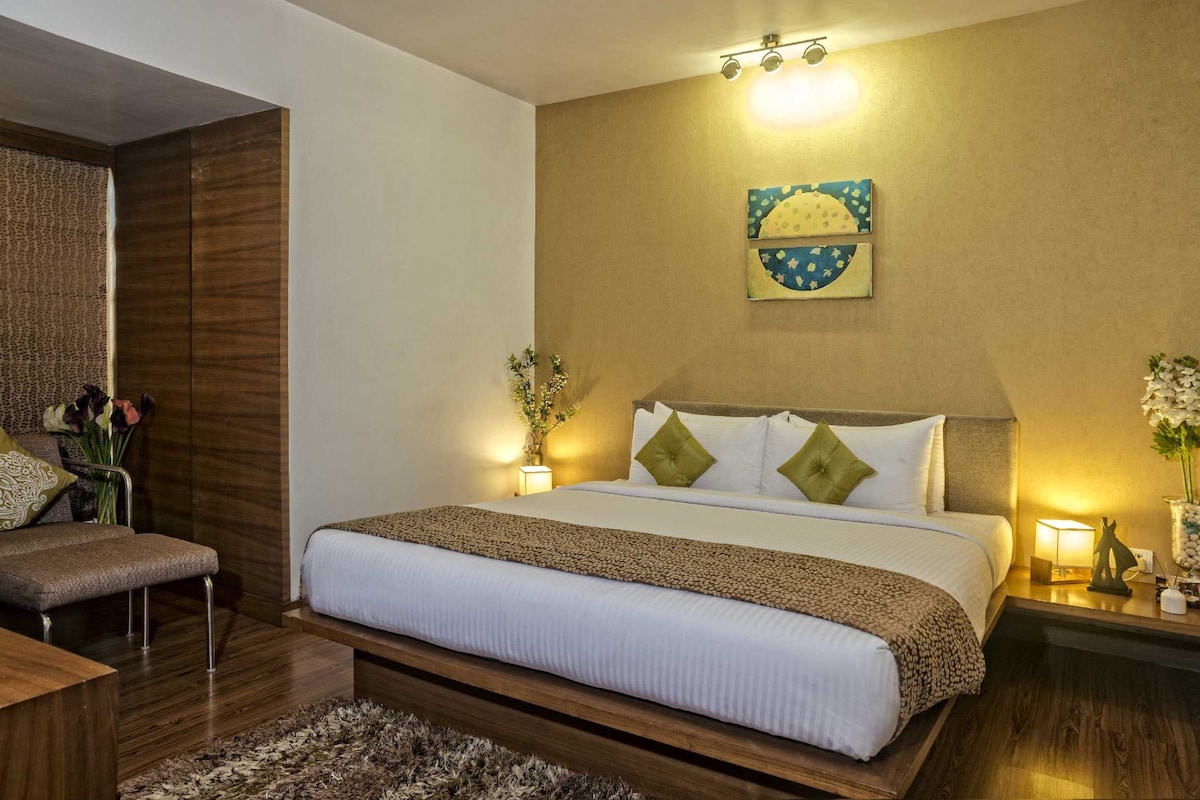 A hotel room with a large bed, a chair, a nightstand, and a wall-mounted artwork.