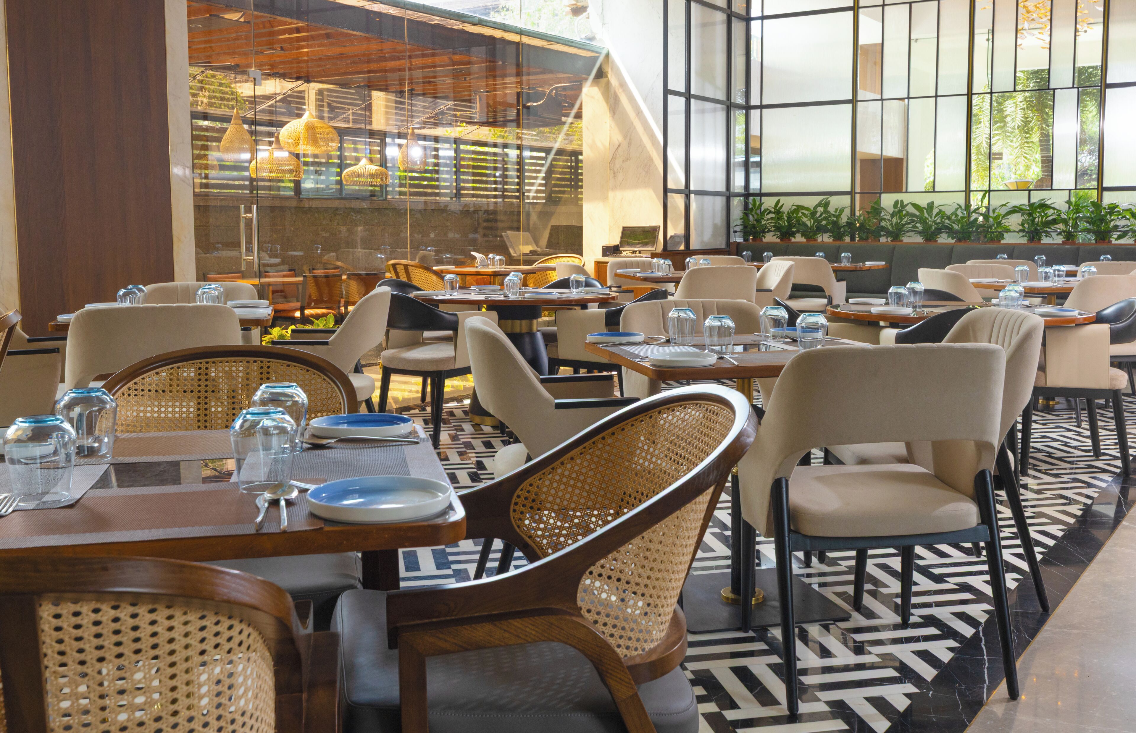 A restaurant with multiple tables and chairs, large windows, and indoor plants.