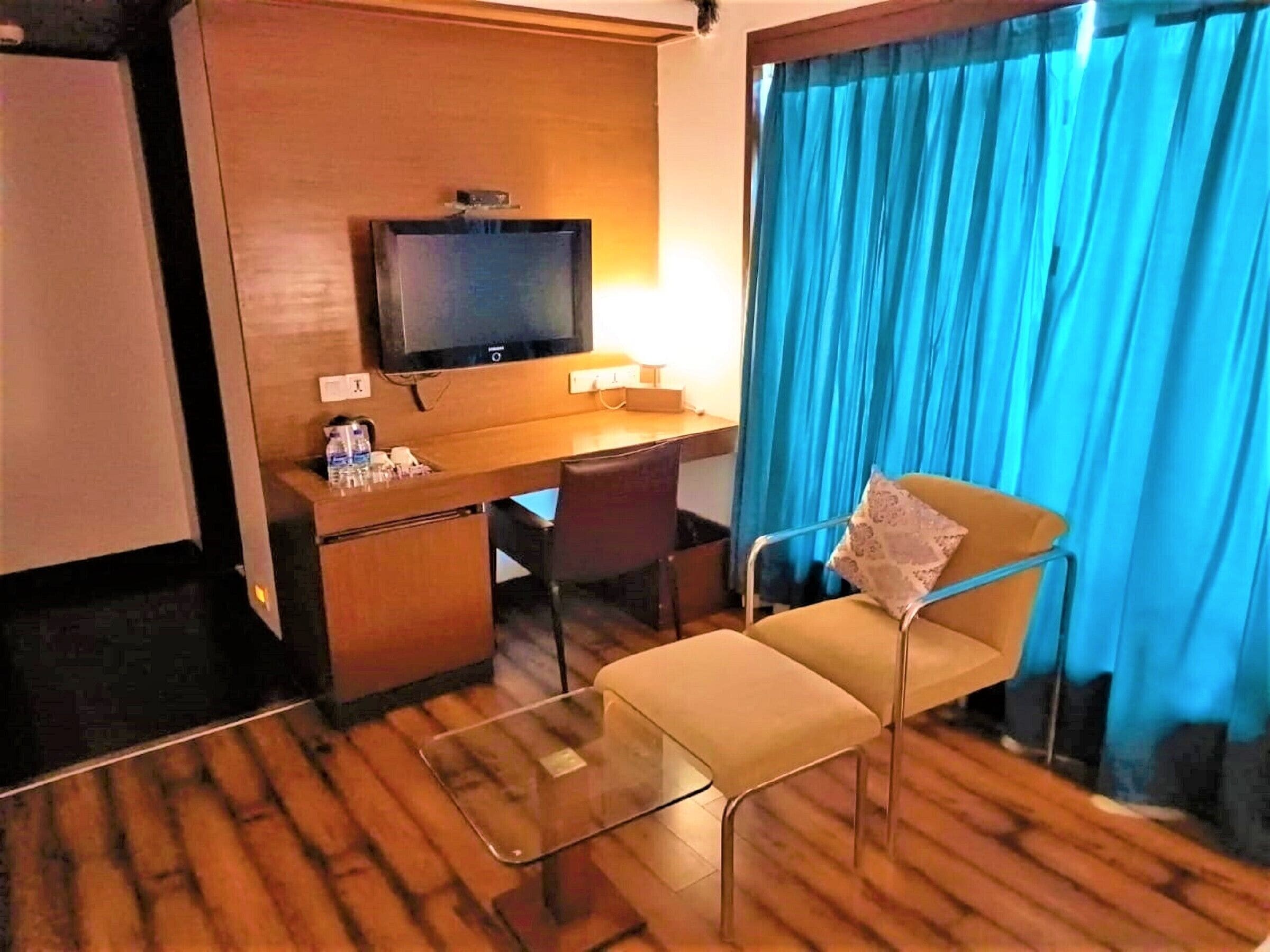 Une chambre d’hôtel avec un bureau en bois, une télévision, une chaise et une fenêtre avec des rideaux bleus.