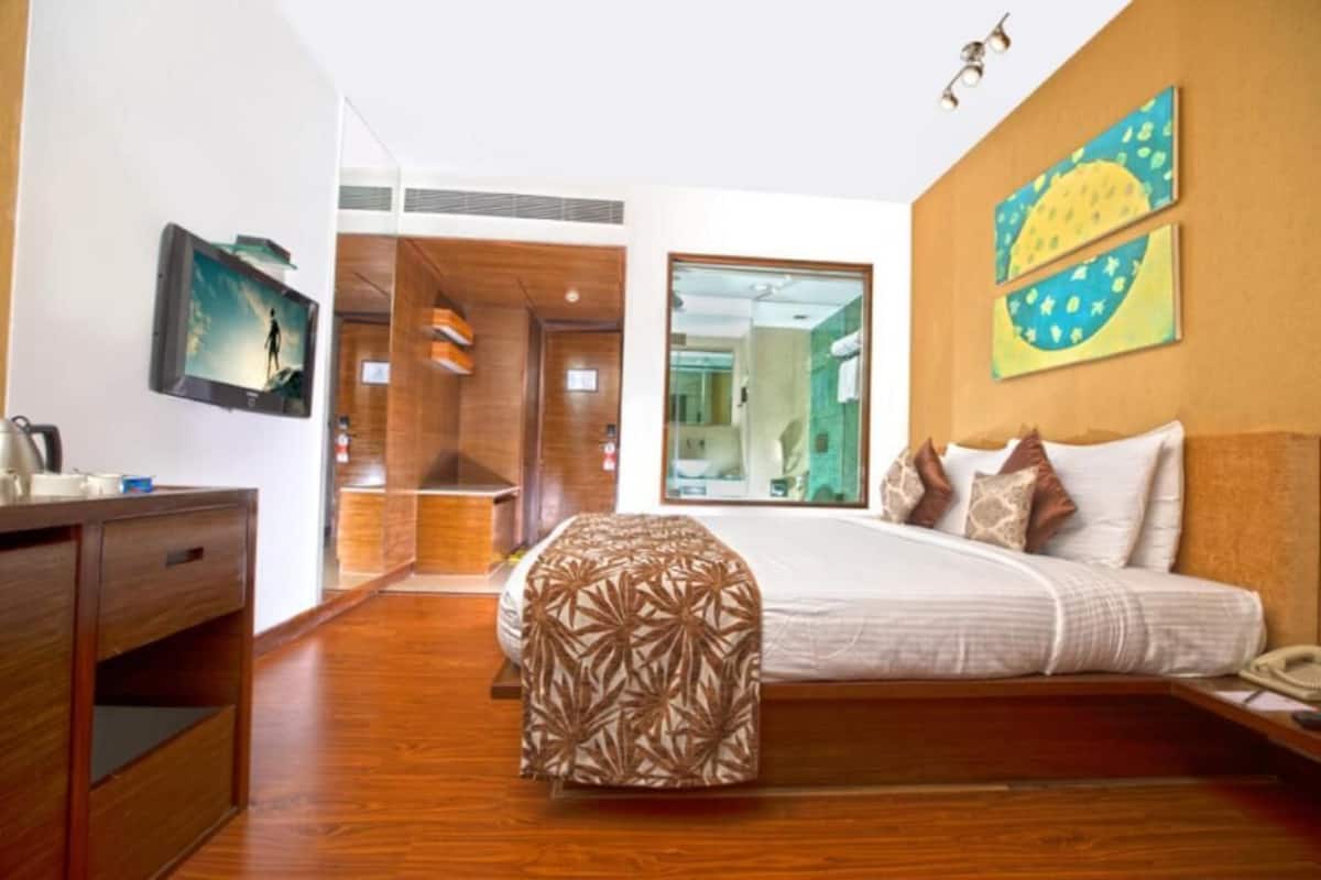A hotel room with a wooden floor, a bed with a patterned bedspread, a desk with a telephone, and a painting on the wall.