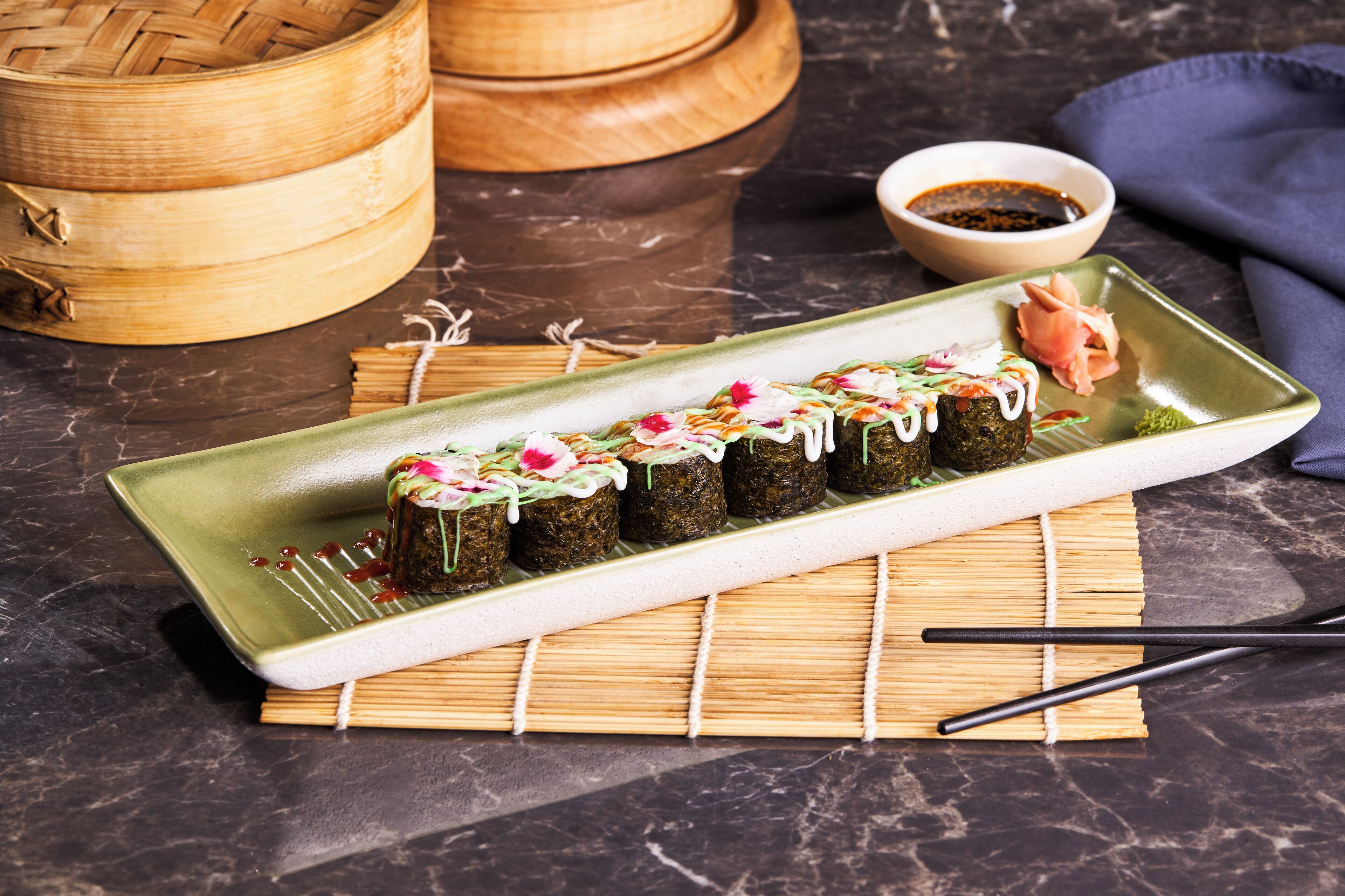 A sushi dish on a rectangular plate with chopsticks and a bamboo mat.