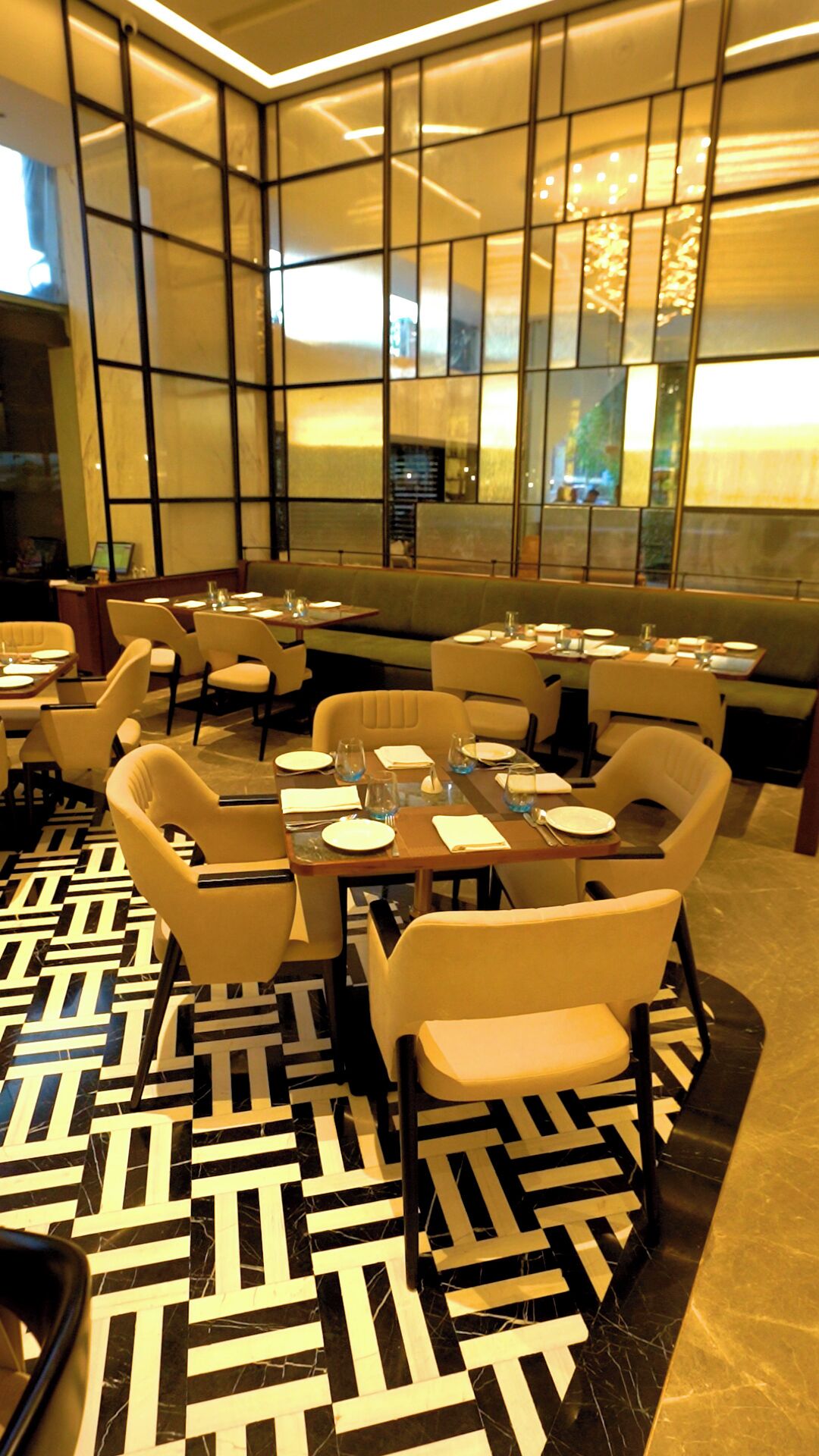 A modern restaurant with a geometric patterned floor, tables set with plates and glasses, and a large window with a view of the city.