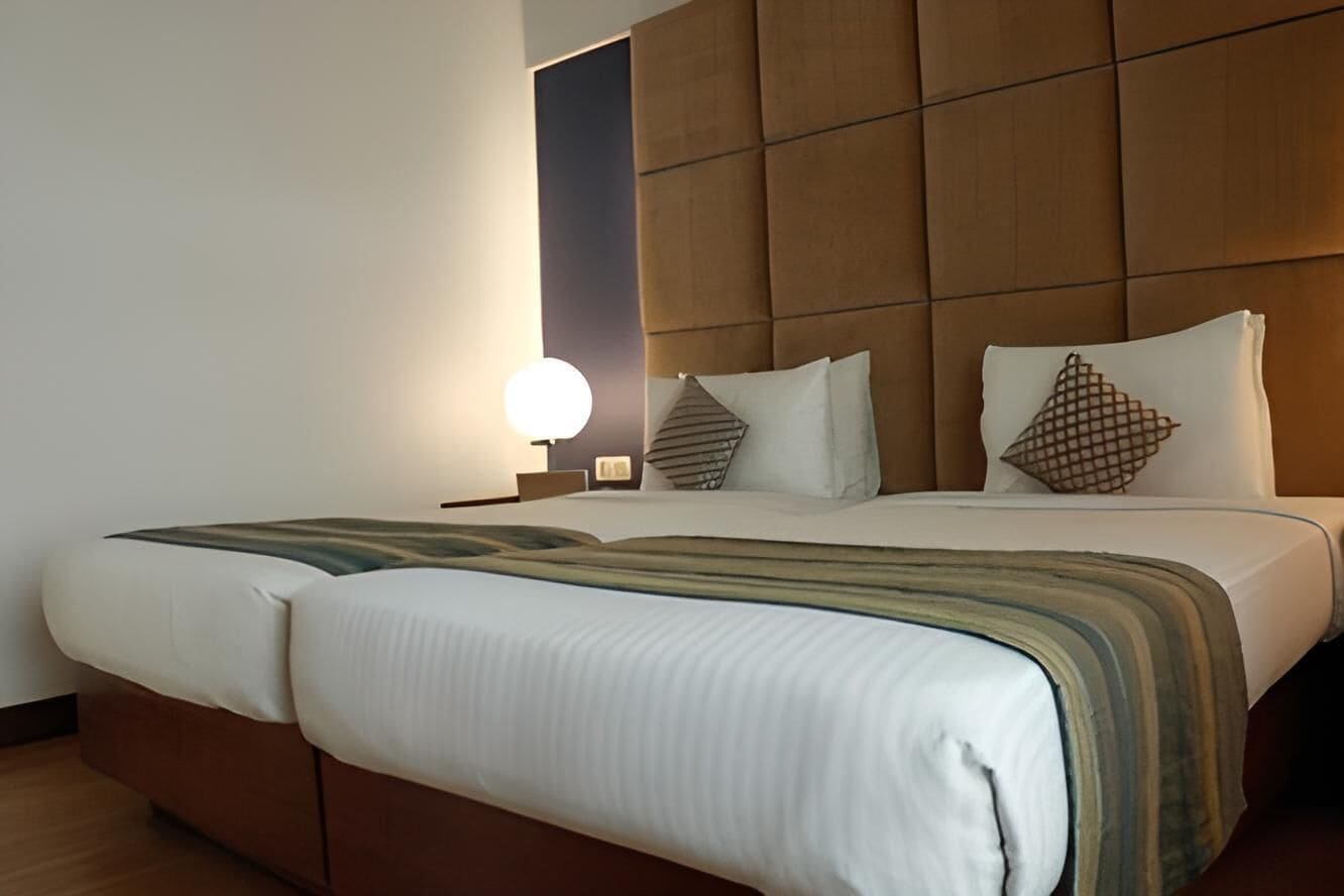 Une chambre d’hôtel avec un grand lit, une tête de lit rembourrée, une table de chevet avec une lampe et une petite table de nuit.
