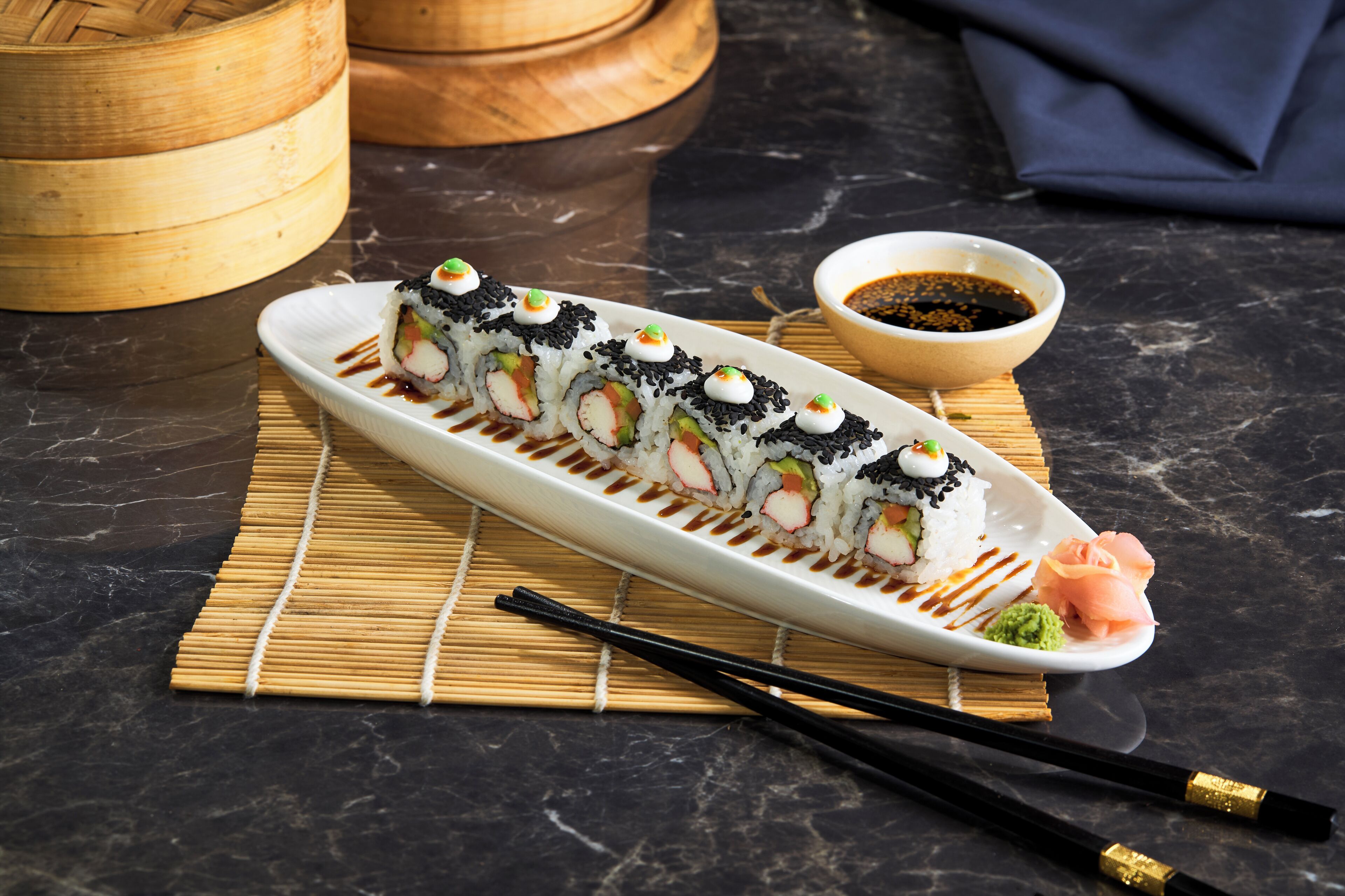 A sushi platter on a white plate with chopsticks and a small bowl of soy sauce.