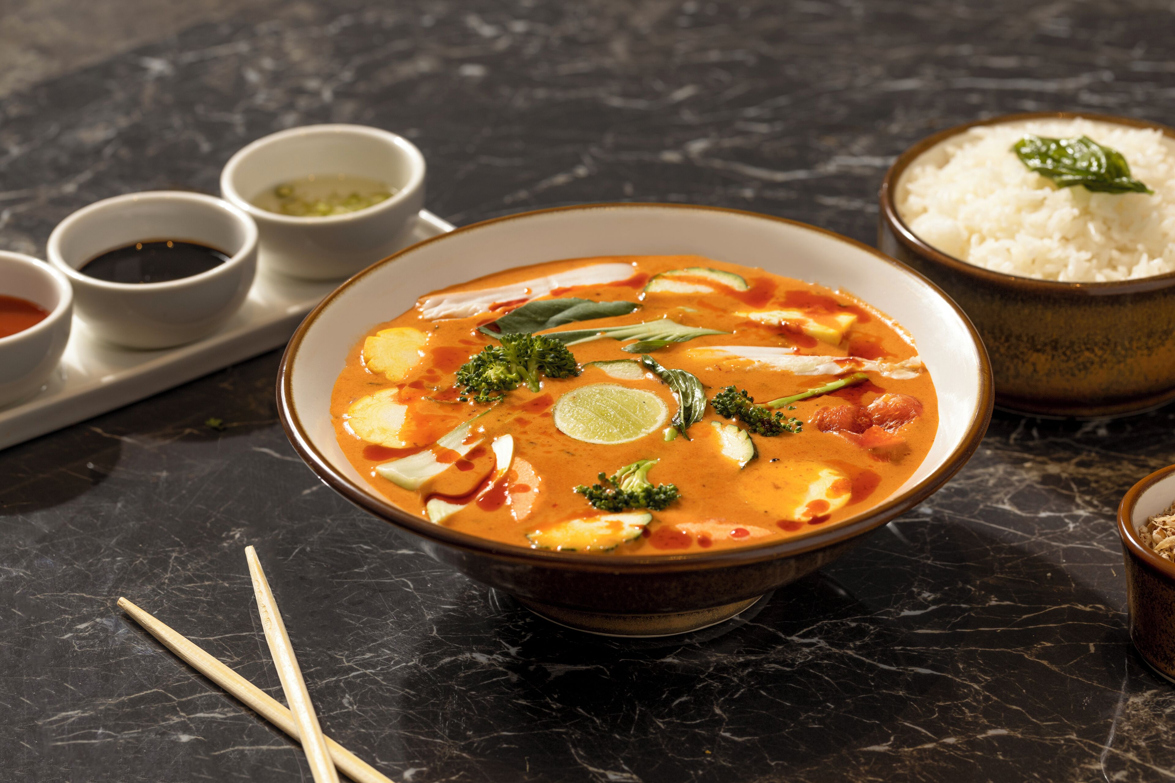 A bowl of soup with various garnishes and side dishes on a marble table.