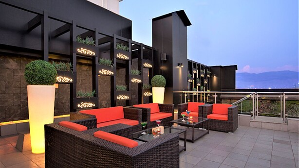 Un lounge sul tetto con mobili in vimini, cuscini rossi e piante in vaso.